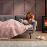 side on image of woman reclining on sofa with a mug, covered in blush pink heated throw