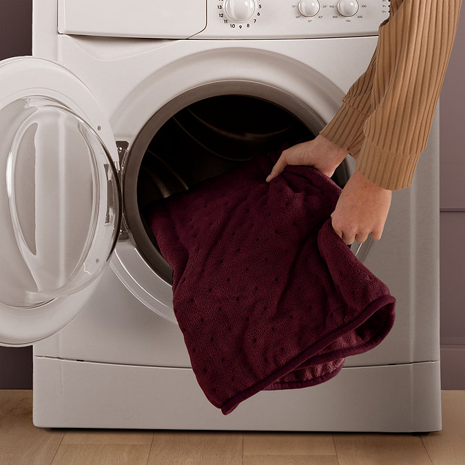 image of burgundy red heated throw being put into a washing machine