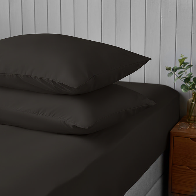 two pillows covered in black pillowcases stacked on top of one another on matching black fitted sheet
