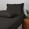 two black pillowcases on pillows at the head of a bed, one stood upright and one led flat on top of the matching black fitted sheet