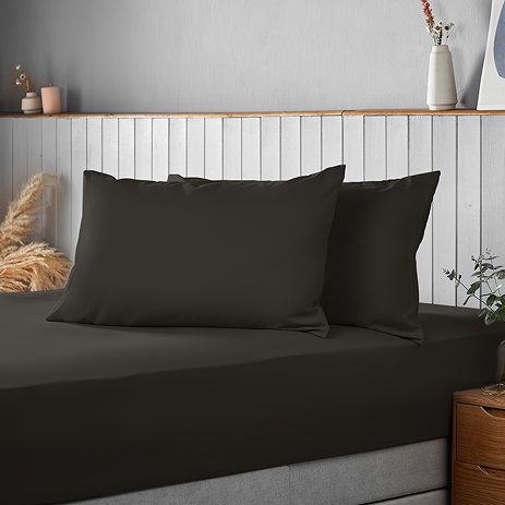pair of pillows covered in black pillowcases resting at head of a bed with matching black fitted sheet