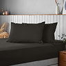 pair of pillows covered in black pillowcases resting at head of a bed with matching black fitted sheet