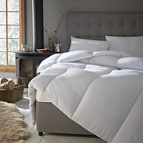 front on image of uncovered duvet on grey velvet bed next to unlit fire