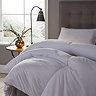 side on close up image of thick uncovered duvet on grey velvet bed next to bedside table with lamp and faux plant