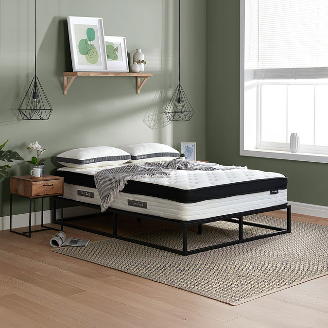 side on image of double mattress on black metal frame against light green wall