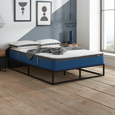 side-on image of double mattress on black bedframe, with top against pale blue wall and light streaming in from the window