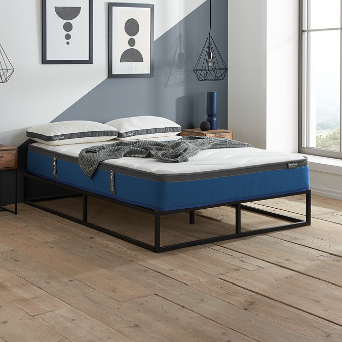 side-on image of double mattress on black bedframe, with top against pale blue wall and light streaming in from the window