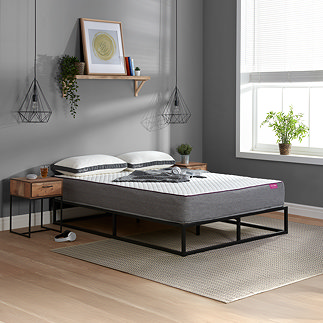 side-on image of double mattress with grey base on a black metal bedframe, pushed up against grey bedroom wall