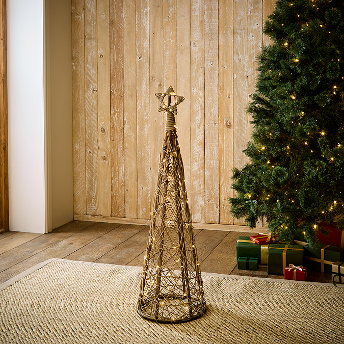small wicker christmas tree with star and LED lighting woven through, stood on rug in living room in front of christmas spruce