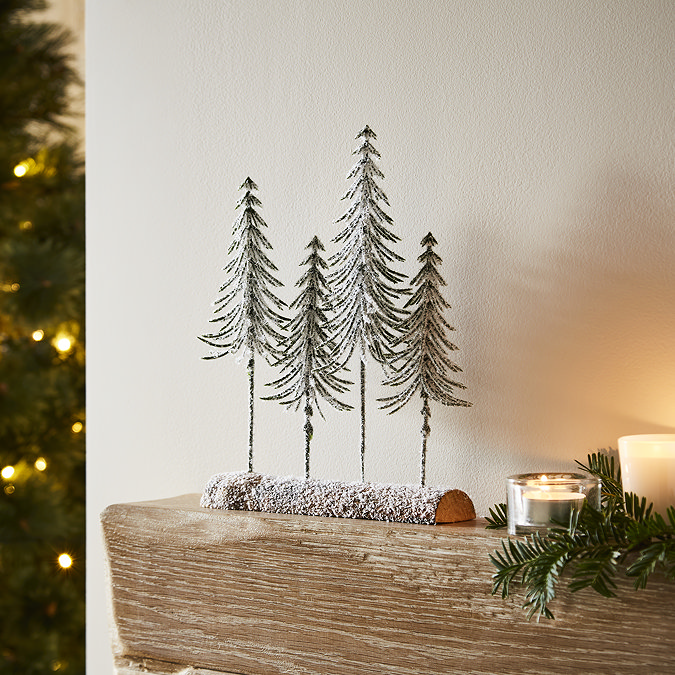 quartet of small snow-dusted spindle trees in a wooden log, displayed on a mantlepiece.