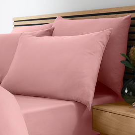 side-on close up image of bed with coral pink fitted sheet and matching pillowcases