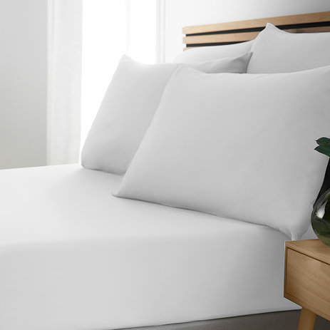 side-on image of bed with no duvet to display white fitted sheet and pillowcases