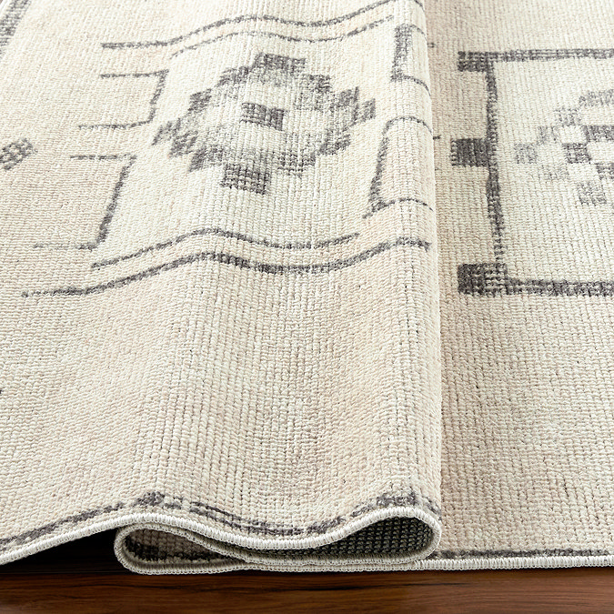 close up image of ivory rug with black scandi geometric pattern, ruched up slightly to show its thinness