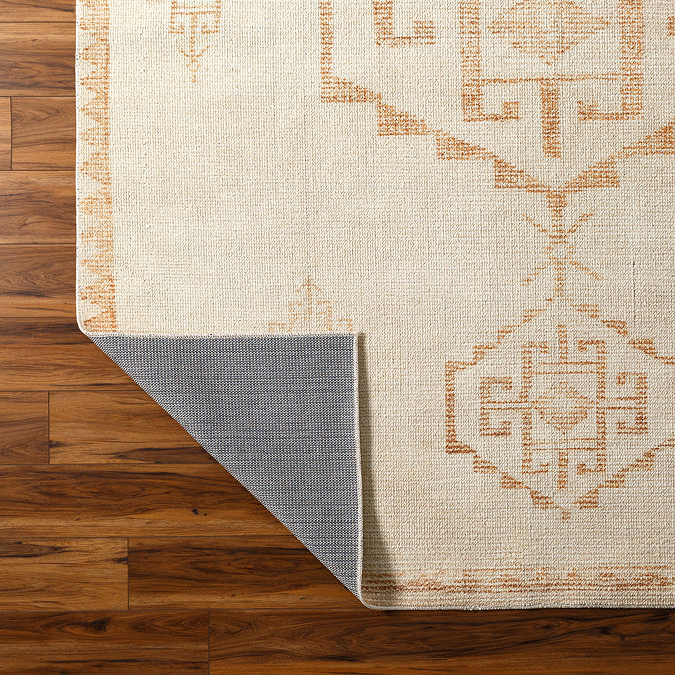 close up image of ivory rug with burnt orange modern scandi pattern, corner folded up slightly to show material underneath