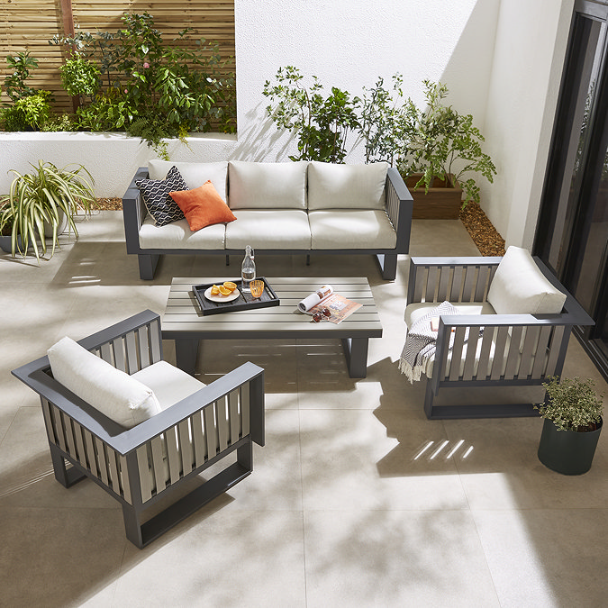 image taken from slightly above of modern slatted grey outdoor lounge set with cream cushions, on patio during a sunny day
