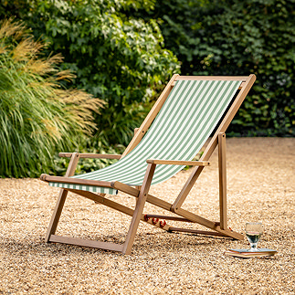 image of green and white stripe deckchair with acacia wood frame, on sandy gravel patio