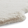 close up on side of beige sheepskin rug with wavy edges and soft pile