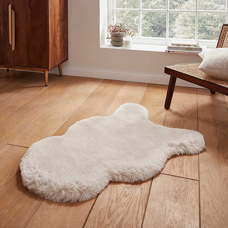 image of fluffy beige faux sheepskin rug on a wooden floor next to a widow with natural light streaming through