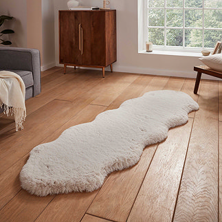 image of double sheepskin rug with wavy edges and soft beige pile, on a wooden floor next to a window with natural light streaming through