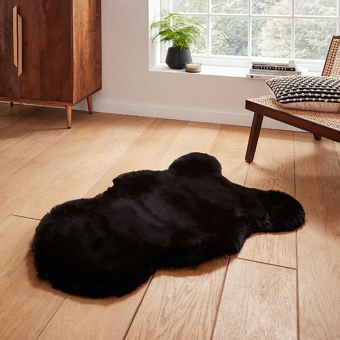 image of small black sheepskin rug on wooden flooring in front of window with light streaming through