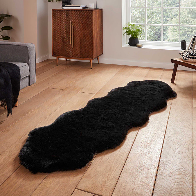 image of black sheepskin rug with wavy edges on wooden flooring in front of window with natural light streaming through