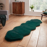 image of long dark green sheepskin rug with wavy edges on wooden flooring in front of window with natural light streaming through