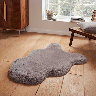 image of long sheepskin grey rug with wavy edges on wooden floor in front of window with natural light streaming through