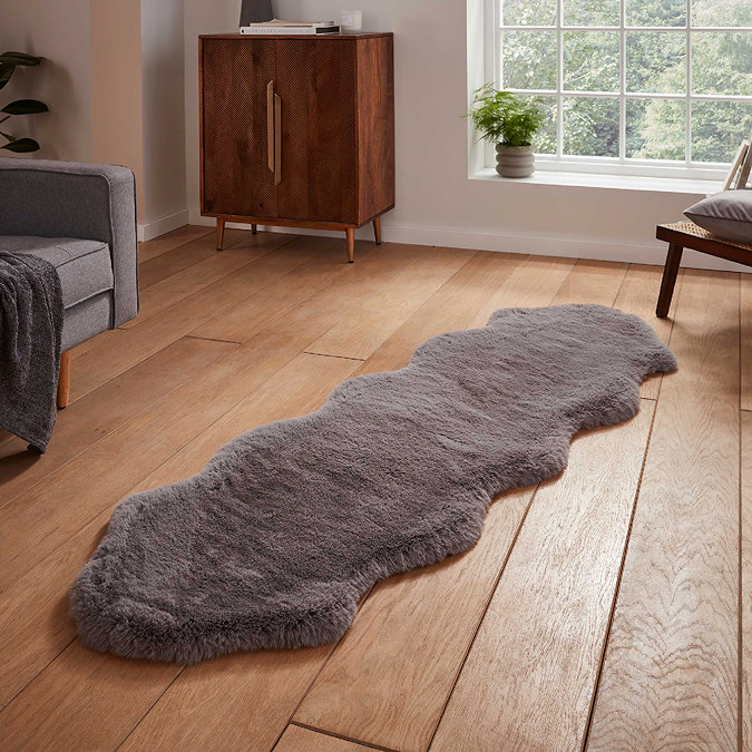 image of longer grey faux fur sheepskin rug on wooden flooring in front of window with natural light streaming through