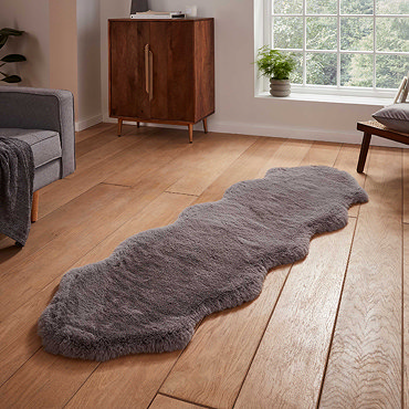 image of long sheepskin grey rug with wavy edges on wooden floor in front of window with natural light streaming through