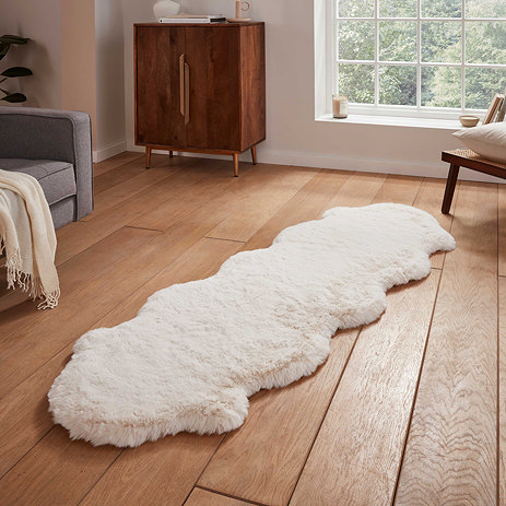 image of long ivory sheepskin rug with wavy edges on wooden flooring in front of window with natural light streaming through