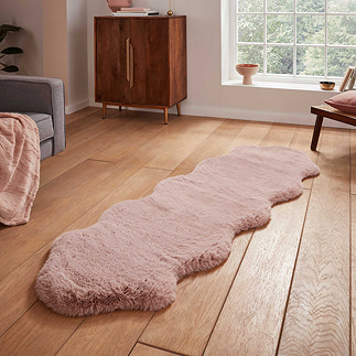 image of long rose pink sheepskin rug with wavy edges on wooden flooring in front of window with natural light streaming through