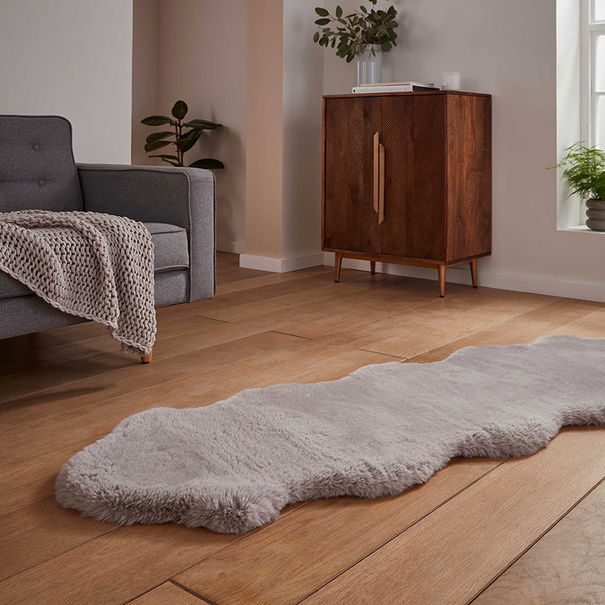 image of long silver sheepskin rug with wavy edges on wooden flooring in front of window with natural light streaming through