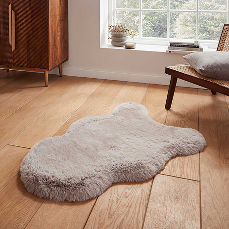 image of short silver sheepskin rug with wavy edges on wooden flooring in front of window with natural light streaming through
