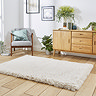 angled image of large soft beige rug on wooden flooring in front of wooden sideboard