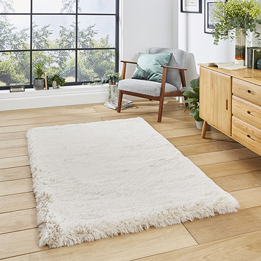 angled image of large soft beige rug on wooden flooring in front of wooden sideboard