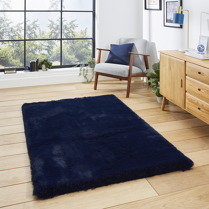 image of navy blue soft rectangle rug on light wooden flooring of modern loft apartment in front of wide window