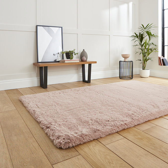 angled image of rose pink soft rug on wooden flooring in front of cream wall and modern dressing table bench with mirror