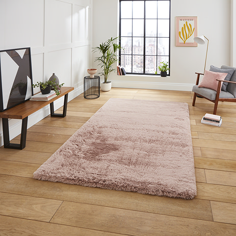 image of rose pink soft rectangle rug on light wooden flooring of modern loft apartment in front of narrow window and grey armchair
