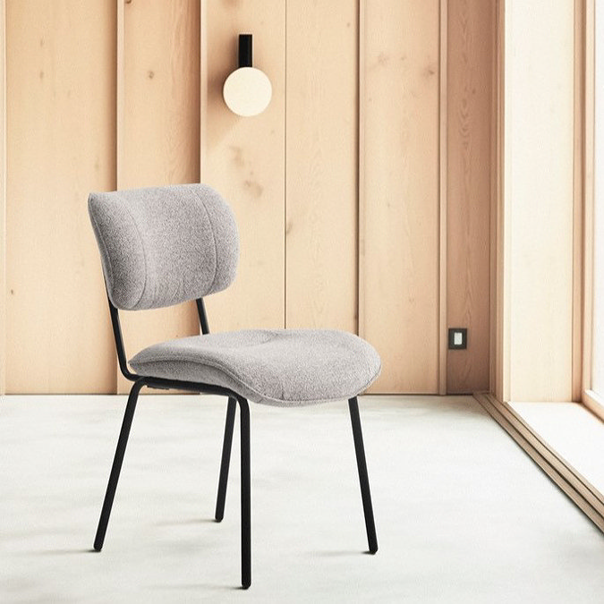 image of off-white fabric dining chair with black steel legs on a stone floor in front of wooden wall and large window