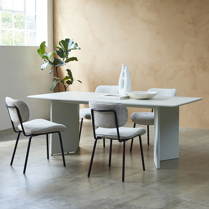 image of four off-white fabric dining chairs with black legs tucked under white rectangle dining table