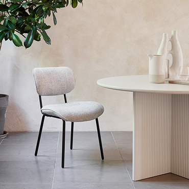 image of off-white fabric dining chair with black steel legs on a stone floor in front of wooden wall and large window