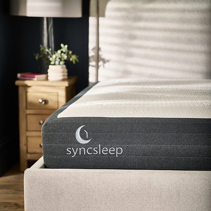 close up image of mattress with dark grey sides on a fabric bed, with 'syncsleep' brand stitched onto it
