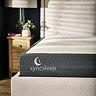 close up image of mattress with dark grey sides on a fabric bed, with 'syncsleep' brand stitched onto it