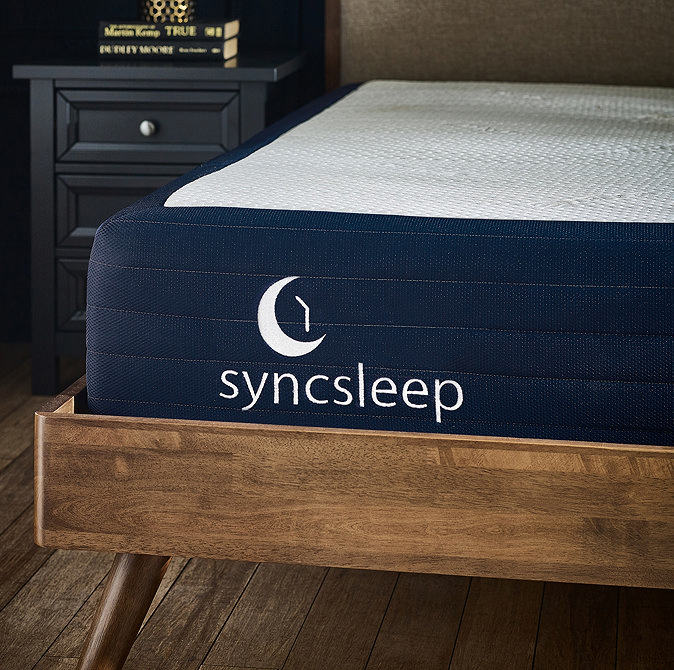 close up image on front left corner of navy blue mattress in a dark wood bedframe, with syncsleep crescent moon logo embroidered in white on it