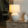 image of latticed ceramic white lamp on a weathered wood sideboard, emitting a warm glow