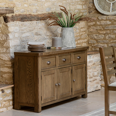 image of dark oak 3 door sideboard pushed against exposed brick wall with faux plant on top