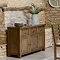 image of dark oak 3 door sideboard pushed against exposed brick wall with faux plant on top