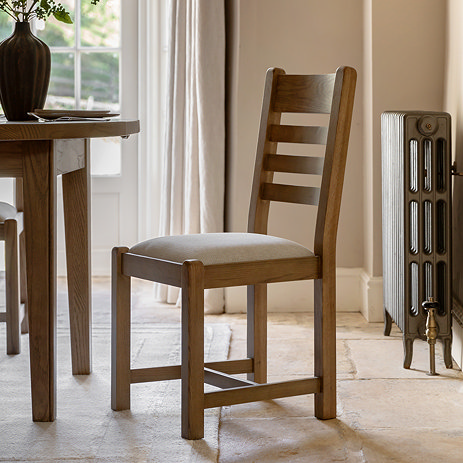 image of dark oak dining chair with padded fabric seat and slatted back, pulled out slightly from matching oak dining table