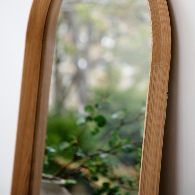 close up image of rounded oak floor length mirror, focus on oak edges an smooth glass