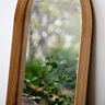 close up image of rounded oak floor length mirror, focus on oak edges an smooth glass